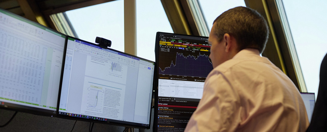 A Norges Bank Investment Management employee working at a desk with multiple screens in the Oslo office.