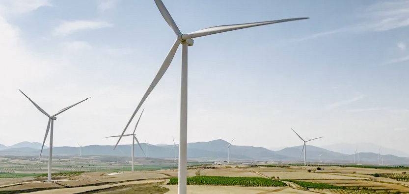 Wind turbines in a rural landscape with fields and distant mountains.