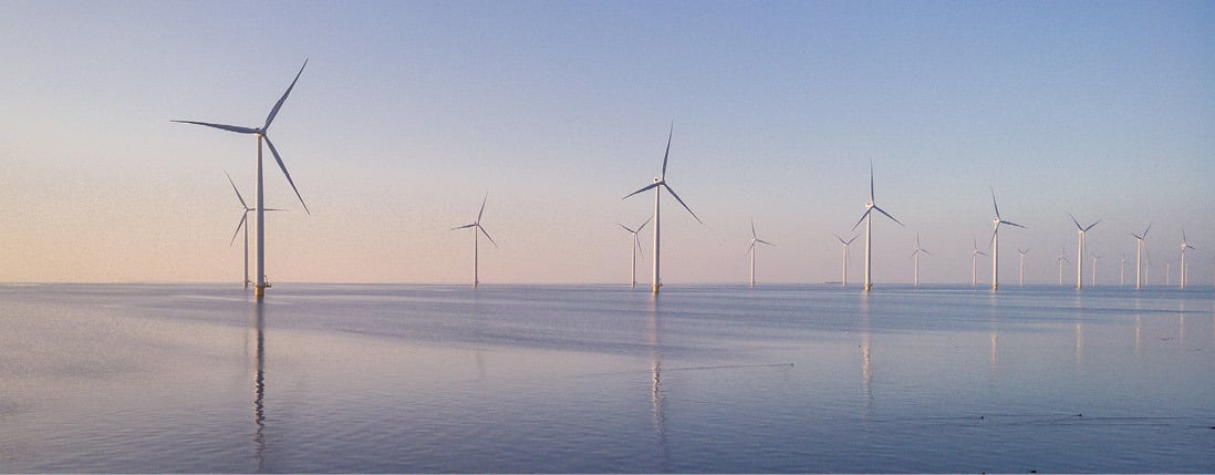 Offshore wind turbines standing in calm waters at sunrise or sunset.