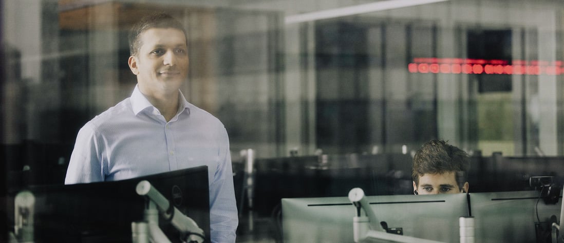 Two Norges Bank Investment Management employees in a trading room, seen through a glass window.