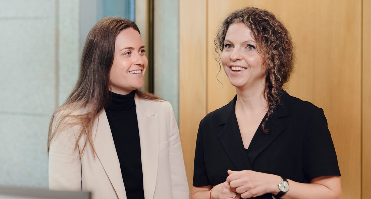 Two female employees at Norges Bank Investment Management conversing in an open-plan office.