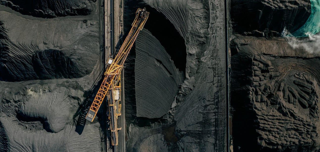 Aerial view of a mine with a yellow excavator in dark soil.