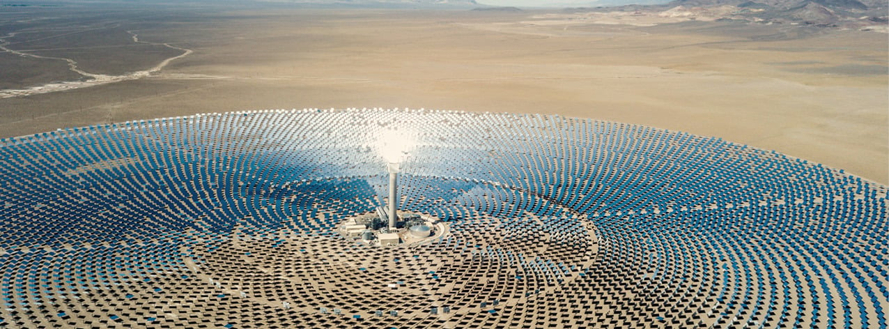 Aerial view of a solar power plant in a desert landscape, with mirrors arranged in a circular pattern.