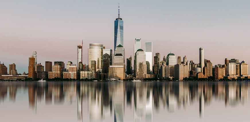 Cityscape of Manhattan reflected in calm water.