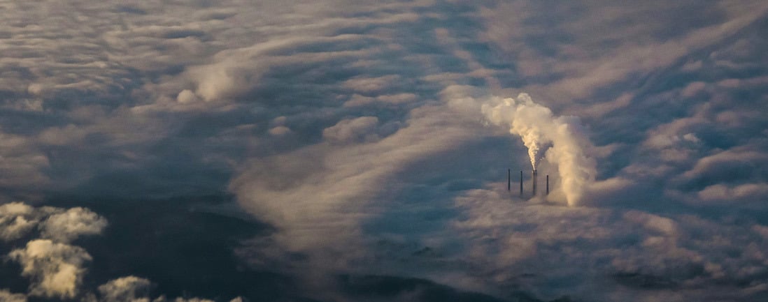 Aerial view of factory chimneys emitting smoke above the cloud cover.